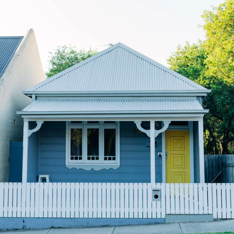 Blue cottage with a white picket fence and yellow door