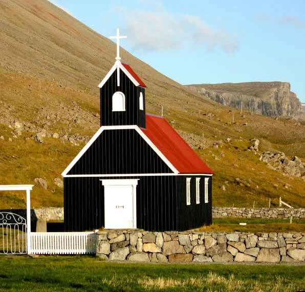 Black wooden chapel with a red roof on a green hillside